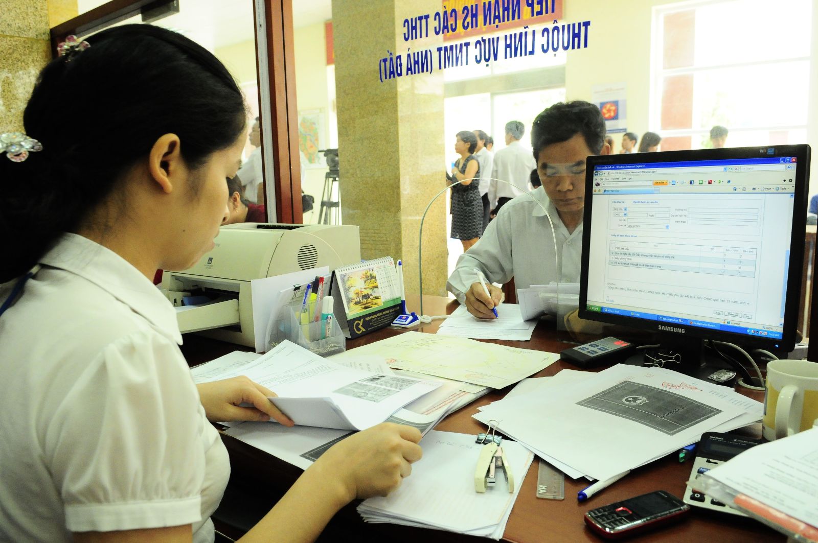 2 người đang trao đổi với nhau, trên tay họ cầm nhiều giấy tờ