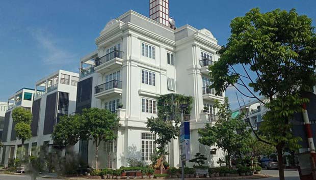 Dãy nhà 3 tầng màu trắng nằm cạnh đường giao thông, nhiều cây xanh.